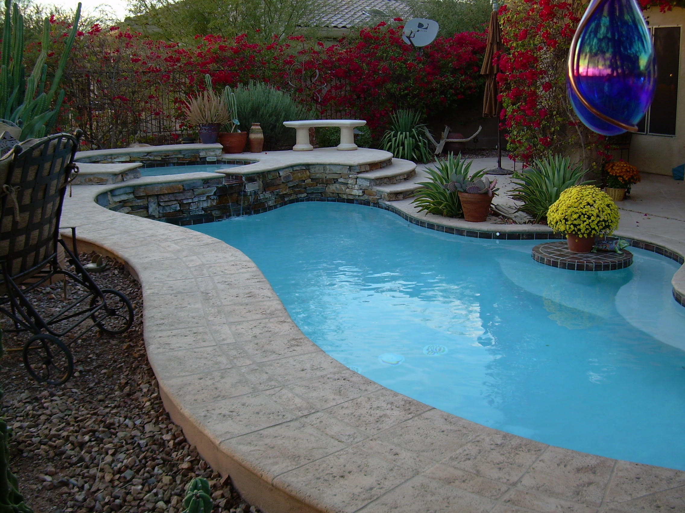 Curved Arizona backyard pool with raised stone spa spillway and colorful desert planting