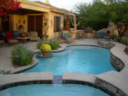 Freeform pool with attached spa, stacked stone wall, and desert landscaping in Arizona