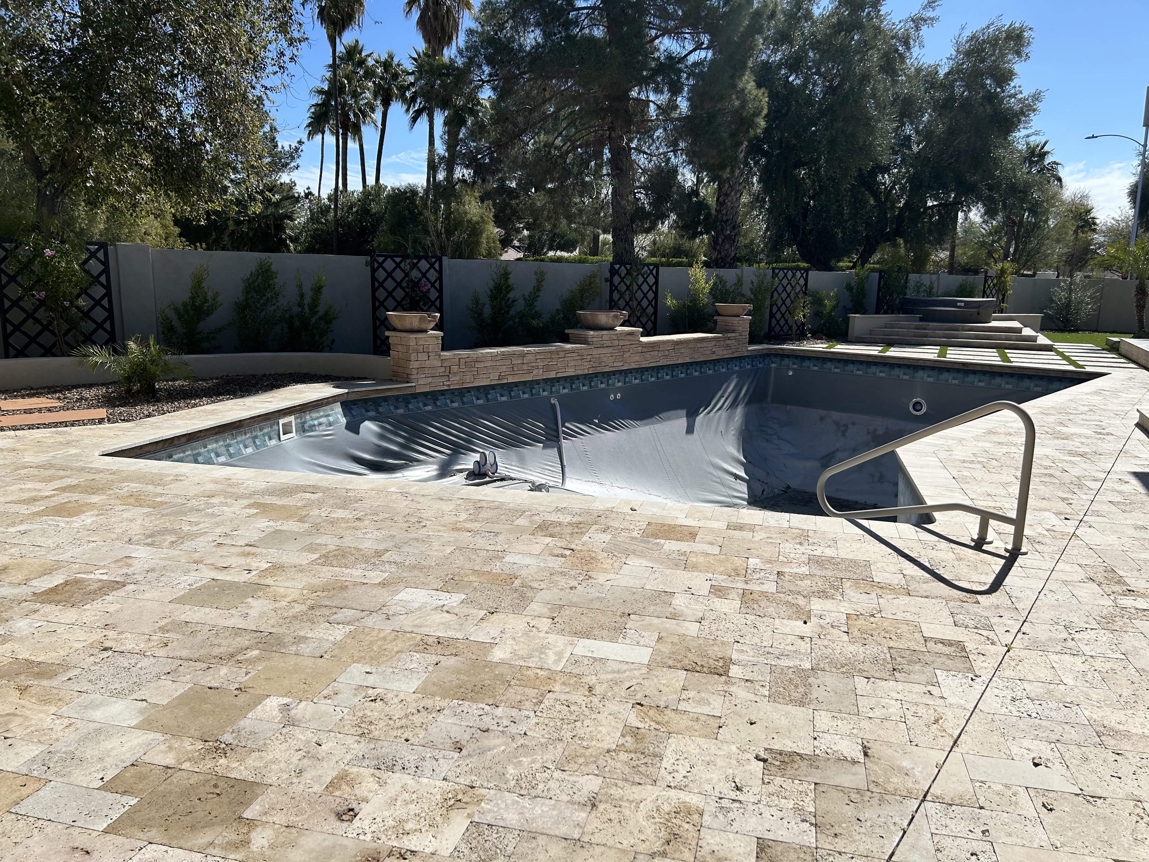 Pool remodel mid-construction with new travertine decking and stone wall being installed in Arizona
